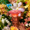 Hand holding a glass of Kin Euphorics Kin Bloom surrounded by flowers Thumb