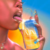 A person holding and licking a can of  Kin Euphorics Actual Sunshine. Can and persons nails are blue and yellow. Person is wearing gold jewelry  Thumb